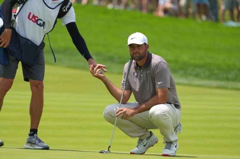 Caddie Ted Scott, left, hands a ball to Scottie Scheffler on the first green during the first round of the U.S. Open