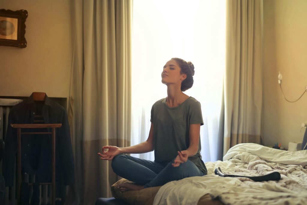 Image of a woman sitting on the end her bed meditating.